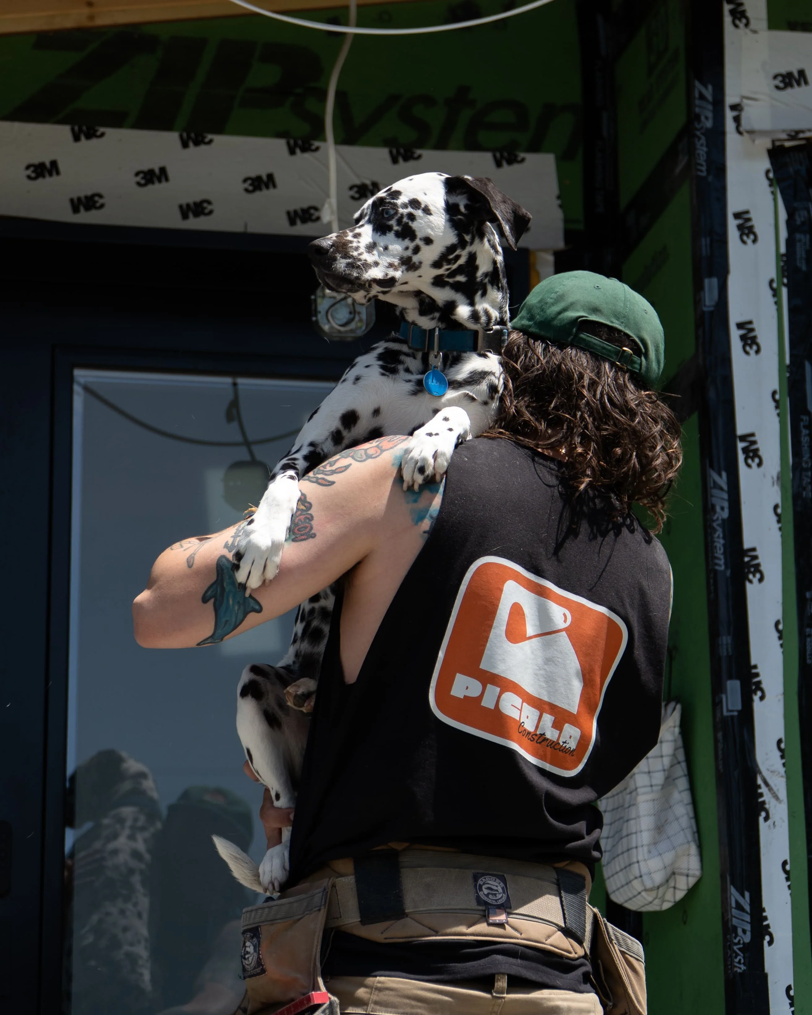 Employé de Construction Picolo portant son chien devant un mur pare-intempéries