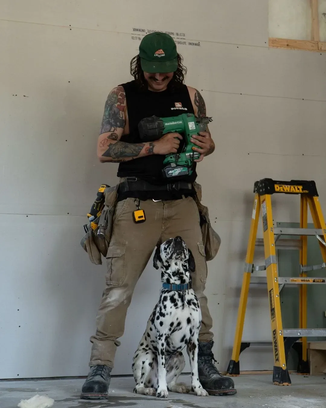 Patrick Lessard sur un chantier, cloueuse en main, avec Picolo le dalmatien assis à ses pieds